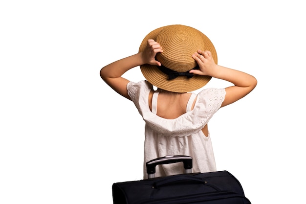 Una niña con un sombrero y una maleta con equipaje, una bolsa de viaje en sus manos mirando hacia adelante