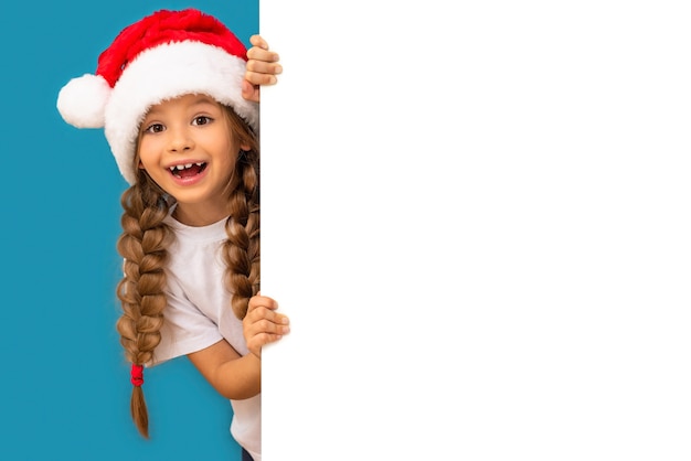 Una niña con un sombrero de Navidad se asoma detrás de la pared.