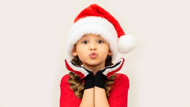 Niña con un sombrero de Navidad en una pared blanca aislada.