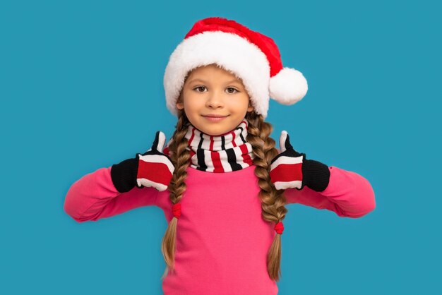 Una niña con un sombrero de Navidad posa sobre una pared azul