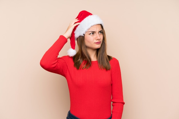 Niña con sombrero de navidad sobre fondo aislado con dudas y con expresión de la cara confusa