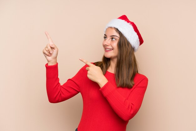 Niña con sombrero de navidad sobre pared aislada señalando con el dedo índice una gran idea