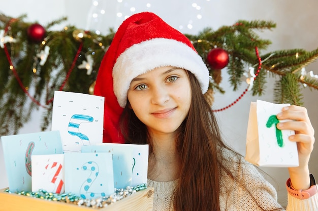 una niña con un sombrero de Navidad tiene un calendario de Adviento en sus manos diy