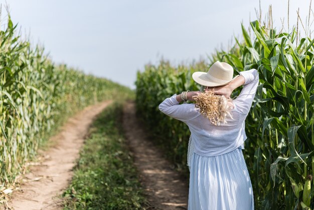 Una niña con un sombrero de paja camina en el campo de maíz