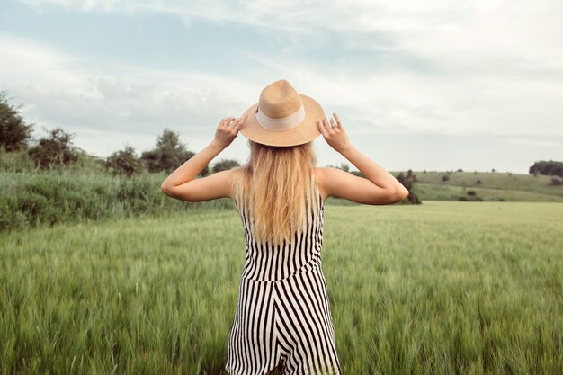 Una niña en un sombrero de paja camina sobre un campo verde al atardecer