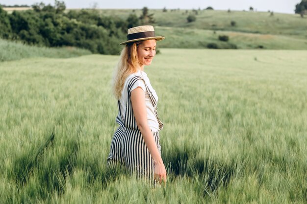 Una niña en un sombrero de paja camina sobre un campo verde al atardecer