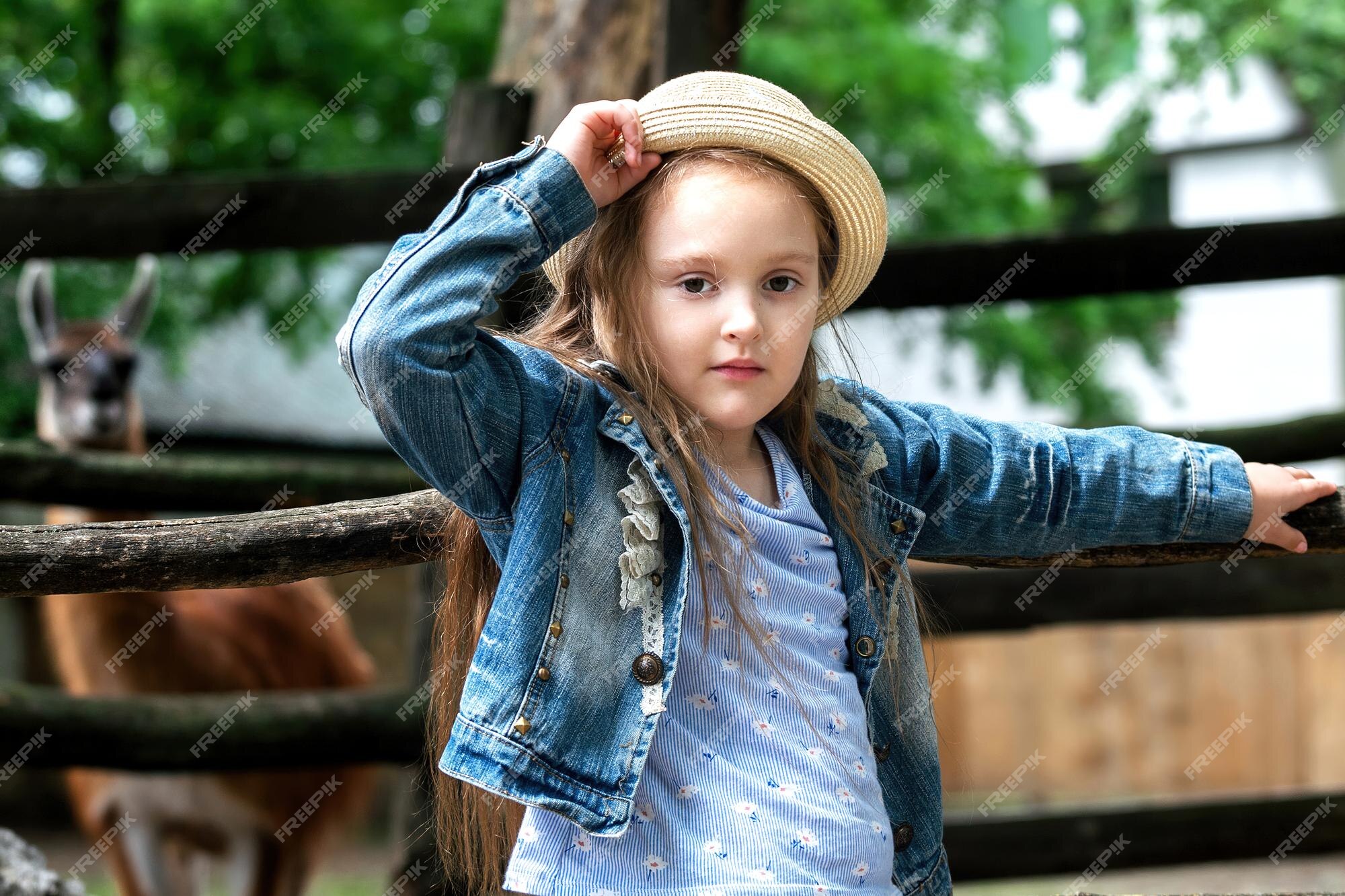 Una niña con un sombrero de paja camina en el zoológico con animales en el  fondo detrás del seto una llama | Foto Premium