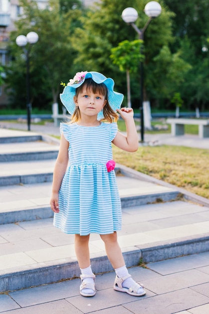 Una niña con un sombrero de paja está parada en los escalones del parque Un niño con un hermoso vestido azul