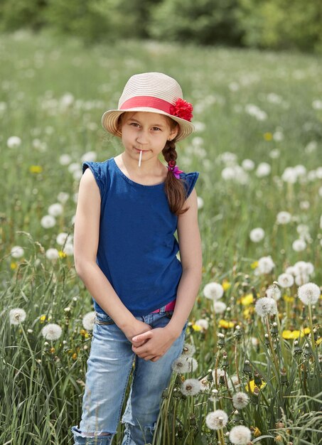 Niña en un sombrero de paja de pie en un prado verde