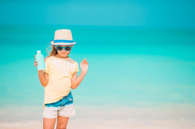 Niña con sombrero de paja en la playa con botella de crema solar. proteccion solar