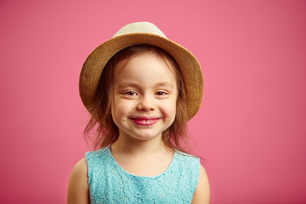 Niña con sombrero de paja y vestido azul se encuentra en rosa aislado Niño feliz anticipa vacaciones