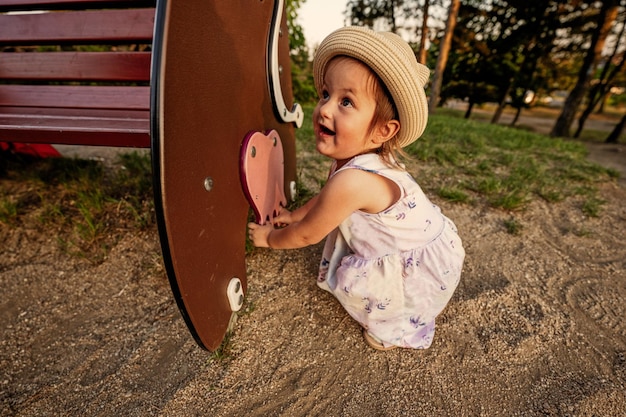 Una niña con sombrero panamá se sentó junto al banco en el patio de recreo al aire libre