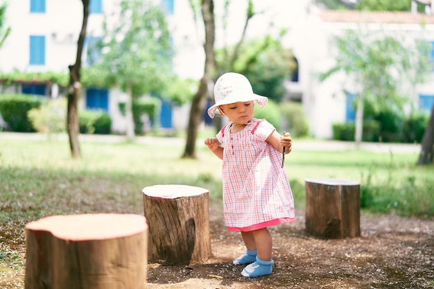 Niña con un sombrero de pie cerca de los tocones en el patio