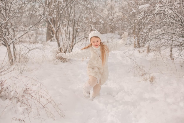 una niña con un sombrero de punto blanco y un suéter corre por un parque nevado