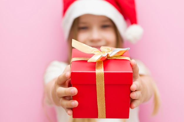 niña con un sombrero rojo de Navidad presenta una caja roja con un lazo dorado, un regalo. Sonrisas El nuevo año es 2021. Cerrar