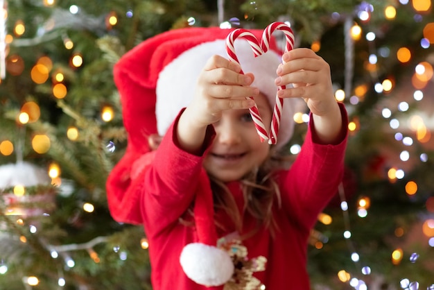 Niña con sombrero rojo de Papá Noel decorando el árbol de Navidad en casa