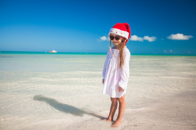 Niña con sombrero rojo santa claus y gafas de sol en la playa