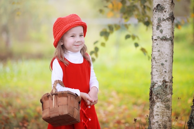 Una niña con un sombrero rojo y vestidos está caminando en el parque. Cosplay para el héroe de cuento de hadas "Caperucita Roja"