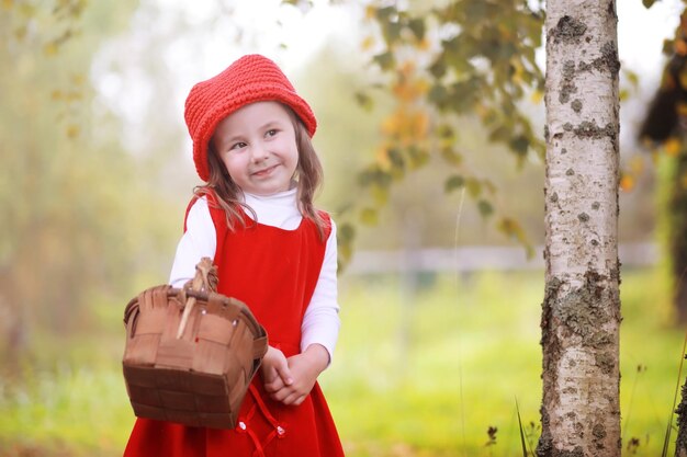 Una niña con un sombrero rojo y vestidos está caminando en el parque. Cosplay para el héroe de cuento de hadas "Caperucita Roja"