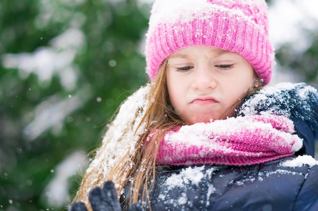 Una niña con sombrero rosa con cara enojada en el parque de invierno