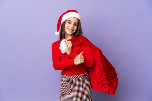 Niña con sombrero y saco de Navidad aislado sobre fondo púrpura orgulloso y satisfecho de sí mismo