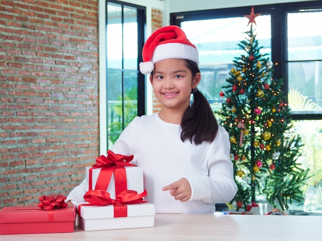 Niña con sombrero de santa con cajas de regalo en casa.