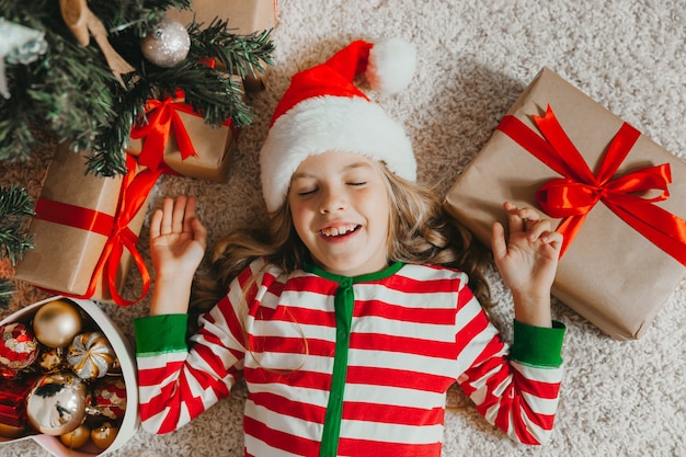 Niña con un sombrero de santa claus se encuentra cerca del árbol de Navidad en casa. vista desde arriba. Navidad.