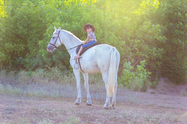 La niña en un sombrero se sienta en un caballo