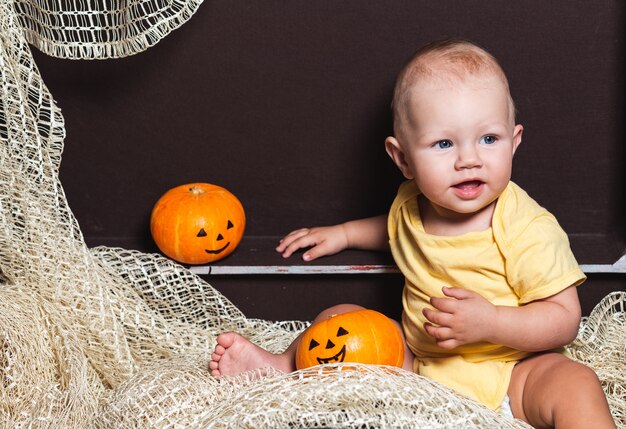 Una niña con un sombrero se sienta en un cofre cerca de una calabaza.