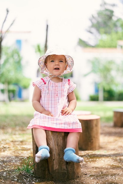 Niña con sombrero se sienta en el tocón de un árbol