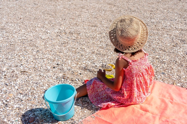 Foto niña con sombrero y vestido jugando en la playa