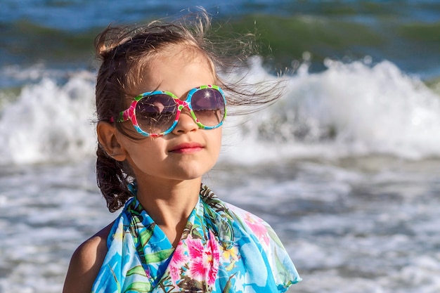 Niña soñadora con los ojos cerrados en gafas de sol en las que el sol se refleja en el mar