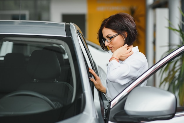 Niña soñando con un coche nuevo inspeccionando un coche blanco nuevo en un concesionario de coches