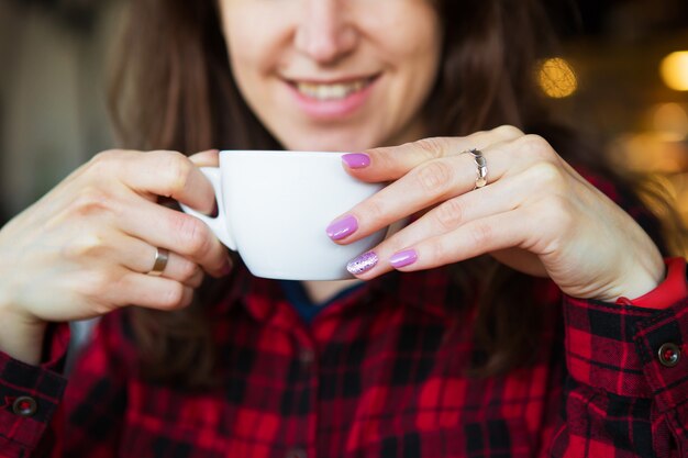 La niña sonríe mientras sostiene una taza de café. De cerca.