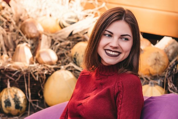 Niña sonríe en el otoño en el fondo de calabazas