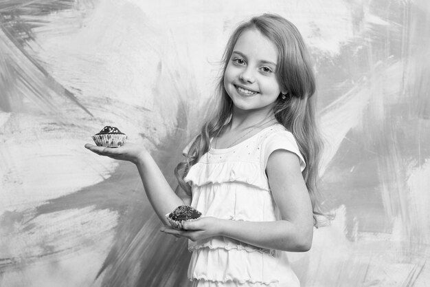 Niña sonriendo con cupcakes en las manos Niño con cabello largo y rubio sosteniendo pasteles Concepto de infancia feliz Confitería postre pasteles comida dieta Vacaciones cumpleaños San Valentín celebración