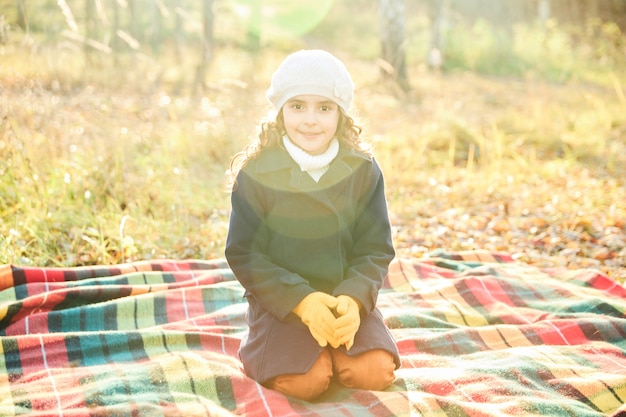 Niña sonriendo mientras está sentado sobre una manta en el parque en otoño. Foto de alta calidad