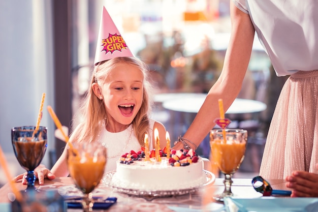 Niña sonriendo y mirando su sabroso pastel de cumpleaños