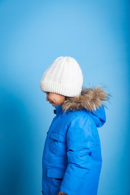niña sonriendo en perfil con chaqueta de invierno azul y sombrero blanco