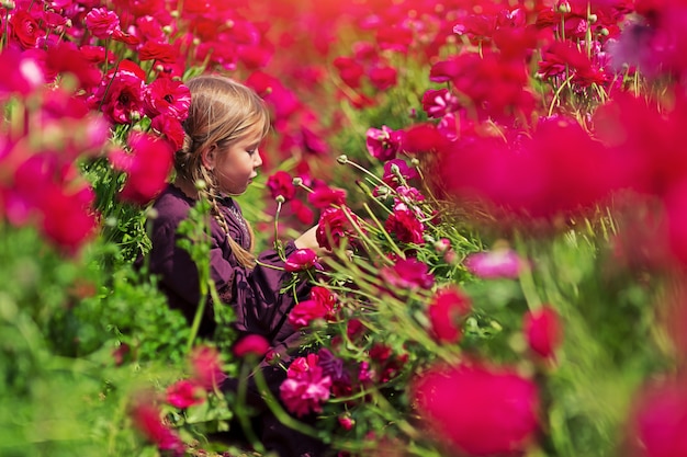 Niña sonriendo y tocando cabezas de hermosas flores vívidas mientras está sentado en el jardín floreciente