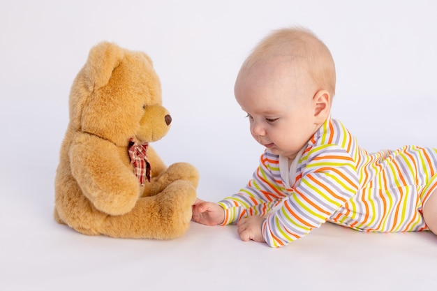 Niña sonriente de 6 meses se encuentra en un traje brillante delante de un suave oso de peluche,