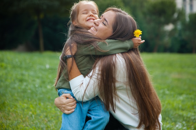 Niña sonriente abrazando a su madre en el parque. Concepto de madre e hija.