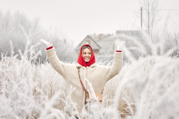 Una niña sonriente con un abrigo de piel blanco posa en arbustos nevados