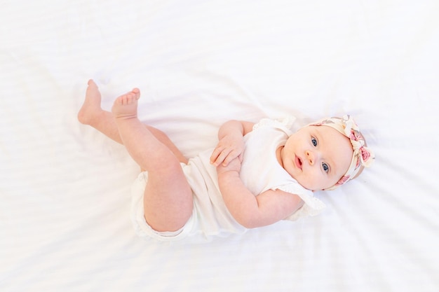 Niña sonriente acostada sobre una cama de algodón blanco en su casa de espaldas