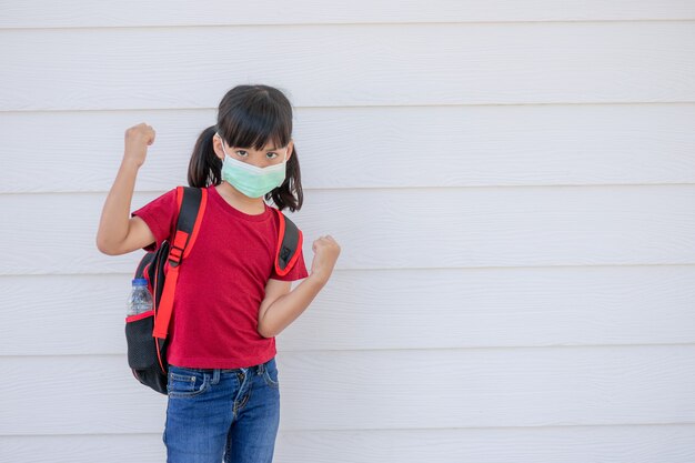 Niña sonriente alegre con mochila grande saltando y divirtiéndose contra la pared blanca. Mirando a la cámara. Concepto de escuela. De vuelta a la escuela