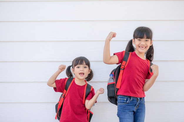 Niña sonriente alegre con mochila grande saltando y divirtiéndose contra la pared blanca. Mirando a la cámara. Concepto de escuela. De vuelta a la escuela