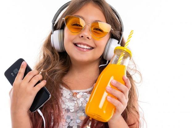 Niña sonriente en auriculares escucha música en gafas naranjas