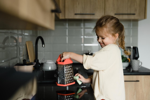 Niña sonriente ayuda con las tareas del hogar lava platos en la cocina