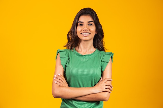 Niña sonriente con los brazos cruzados sobre fondo amarillo.