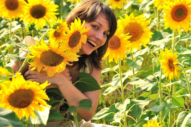 niña sonriente con cabello castaño en el campo de flores sosteniendo girasol en la mano y mirando